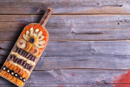 Artistic colorful arrangement of dried produce arranged on a wine bottle shaped bamboo cutting board placed on a rustic wooden table with peeling paint, overhead view