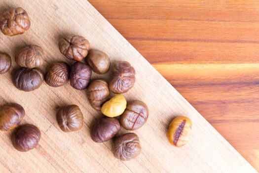 Delicious freshly roasted whole chestnuts scattered on a diagonal wooden board on a wood table with copy space, view from above