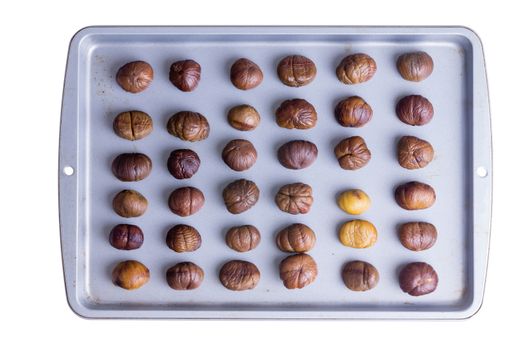 Whole roasted chestnuts neatly arranged in rows on a roasting tray for a delicious autumn snack , overhead view isolated on white