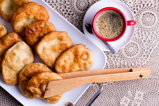 Traditional Turkish pisi halka, or fried golden dough, served on a tray with a freshly brewed cup of frothy black coffee, viewed from overhead with wooden tongs for serving