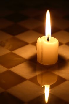 Closeup of one lighting candle on stone chessboard