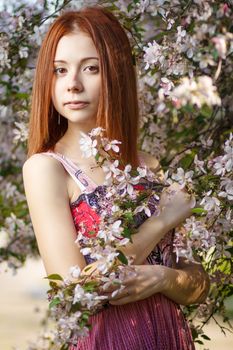 Beautiful redhead girl walking under the rays of the sunset in summer spring blooming forest