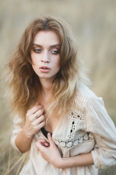 Young sexy woman model in jeans shorts and blouse posing for fashion portrait outside in a field at golden hour sunset