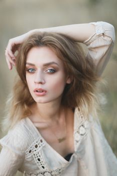 Young sexy woman model in jeans shorts and blouse posing for fashion portrait outside in a field at golden hour sunset