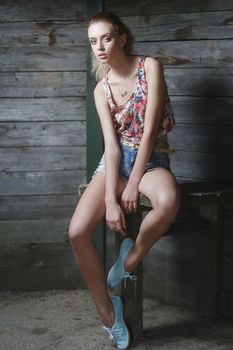 Young sexy woman model in jeans and tank top posing for fashion portrait near old weathered wooden wall outside