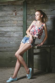 Young sexy woman model in jeans and tank top posing for fashion portrait near old weathered wooden wall outside