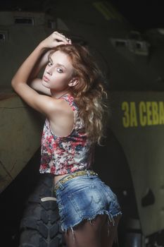 Young sexy woman model in jeans and tank top posing for fashion portrait near old weathered wall outside