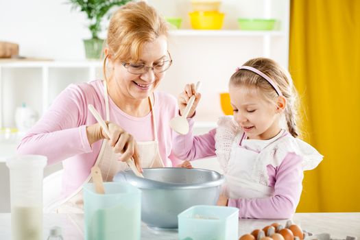 Beautiful happy grandmother learning her granddaughter to Baking in the kitchen.