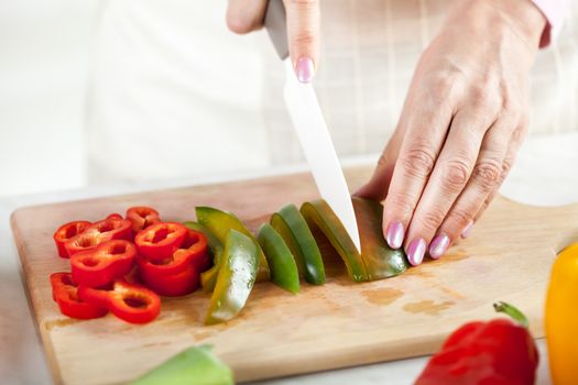 Senior female Hands Cutting green peppers on the kitchen board.