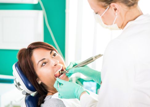 Female dentist with dental drill repairing tooth on the female patient in the office.