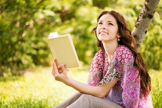 Beautiful Girl with a book in the park sitting on the grass and Expressing Positivity.