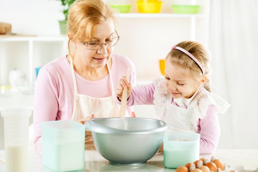 Cute little girl pours flour into a bowl, making Dough in a kitchen. 