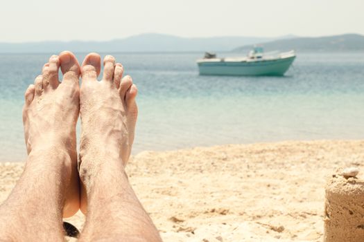 Man with sandy feet relaxing on a beach. Close-up with foot.