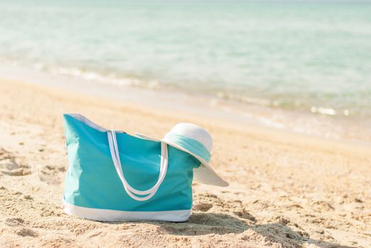 Turquoise bag and white hat on the beach.