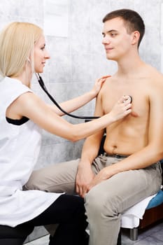 Young female doctor examining young man with stethoscope