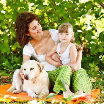 Beautiful mother and daughter relaxing in nature with their dog