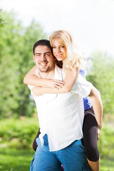 Young man Carrying On Shoulders a beautiful girl in nature