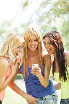Three beautiful girls with mobile phone reading sms at nature