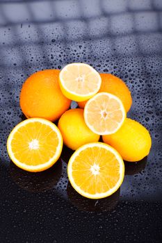 Juicy delicious oranges and lemons on reflective table with water drops