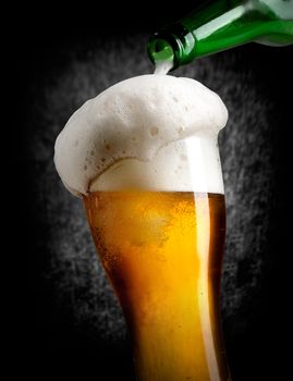 Beer pouring into glass on black background