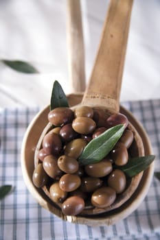 Presentation of a small group of black olives on wooden ladle
