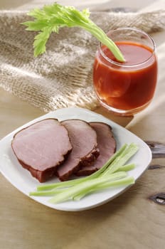 Chunks of pork on the plate and tomato juice with celery in the glass, the morning light, bokeh, defocused background.