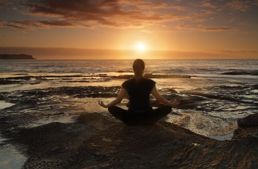 Female sitting by the ocean at sunrise meditating, wellness, health, spirituality.