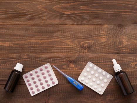 medications or tablets and drops and electronic thermometer on a dark wooden background with copy space. Flat lay or top view