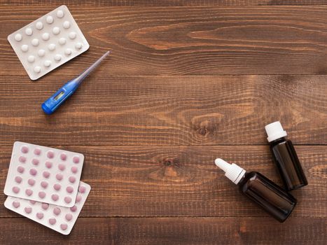 medications or tablets and drops and electronic thermometer on a dark wooden background with copy space. Flat lay or top view