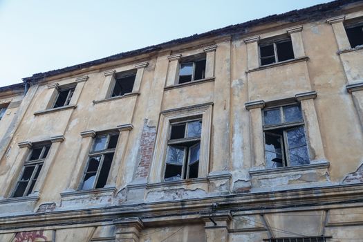 Bottom view of destroyed abondoned yellow stone building with broken windows, on bright blue sky background.