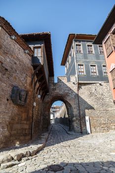 Front view of historical Hisar Gate with pathway and brown and blue old buildings around in Plovdiv old town, on bright blue sky background.