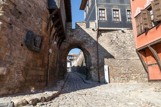 Front view of historical Hisar Gate with pathway and brown and blue old buildings around in Plovdiv old town, on bright blue sky background.