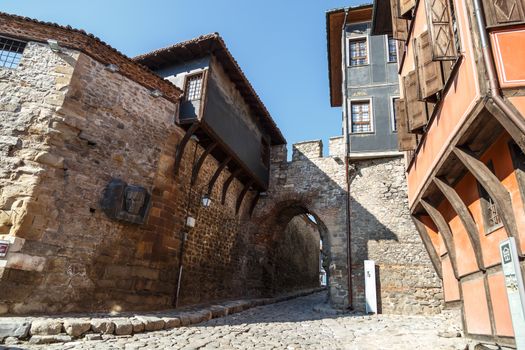 Front view of historical Hisar Gate with pathway and brown and blue old buildings around in Plovdiv old town, on bright blue sky background.