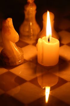 Set of chess pieces made from onyx against lighting candle on chessboard