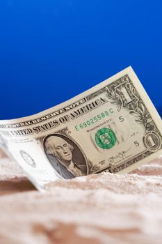 One dollar bank note on sand against blue background