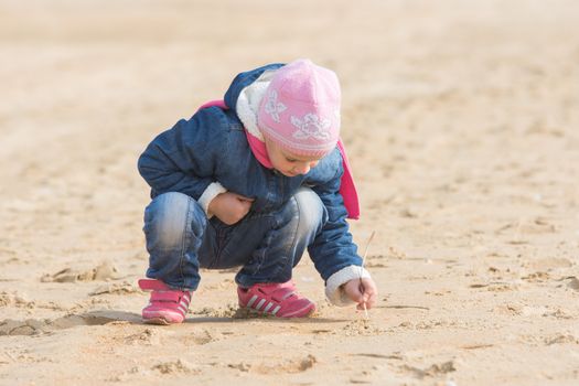 Five-year girl in the spring of the pen draws on the sand by the sea