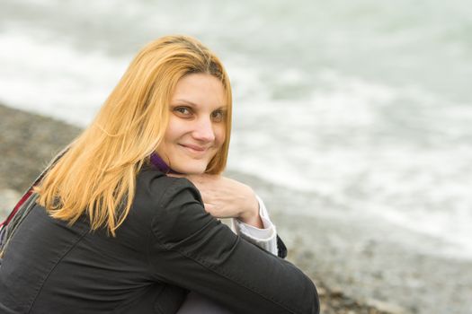 Portrait of sitting on the beach smiling young woman in cold weather