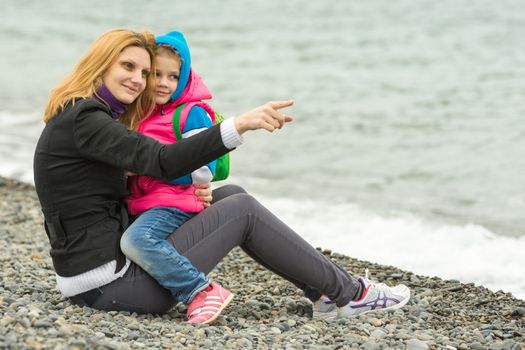 Mom sitting on the beach on a cool day that shows the distance to a daughter sitting on her hands