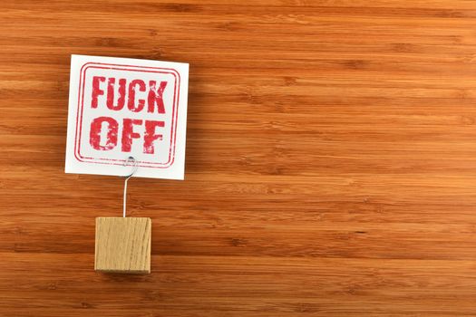Fuck off red rude stamp, one single white paper note with wooden holder on bamboo wooden background for presentation