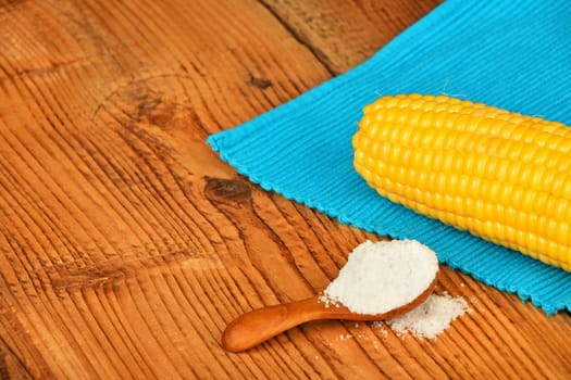 One open fresh yellow corn cob and salt in scoop with blue cloth napkin on brown vintage wooden surface