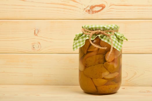 One glass jar of homemade pear compote with green checkered textile top decoration at beige painted vintage wooden surface