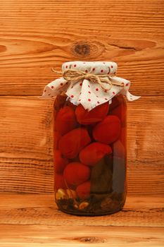 One big glass jar of homemade pickled tomatoes with dotted textile top decoration at brown vintage wooden surface