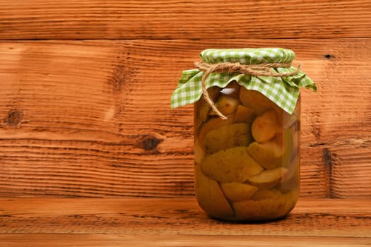 One big glass jar of homemade pear compote with green checkered textile top decoration at brown vintage wooden surface