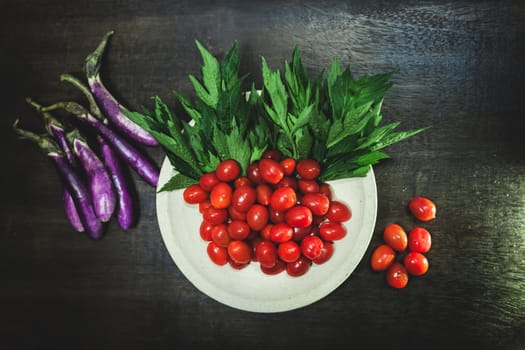 Small tomatoes and green vegetable on rustic black wooden background.