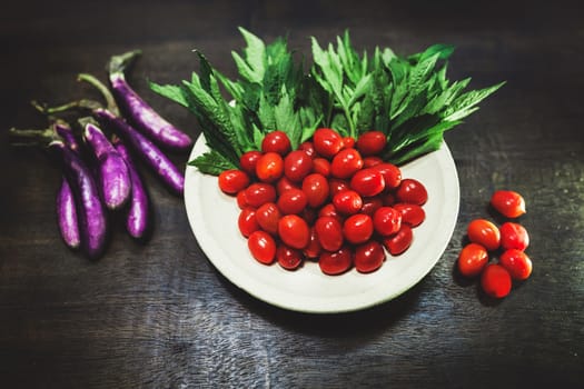 Small tomatoes and green vegetable on rustic black wooden background.