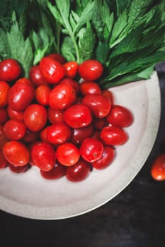 Small tomatoes and green vegetable on rustic black wooden background.