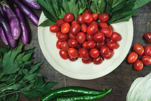 Small tomatoes and green vegetable on rustic black wooden background.