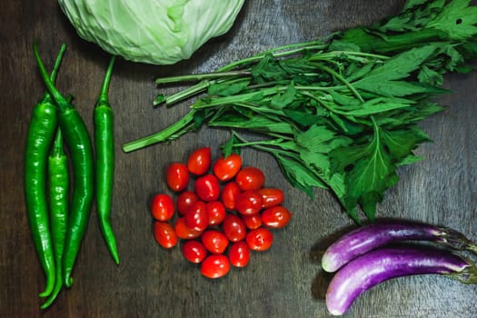 Small tomatoes and green vegetable on rustic black wooden background.