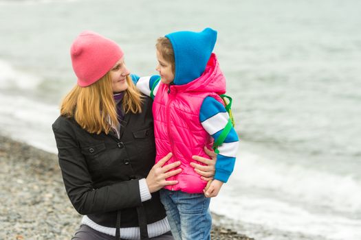  Mother hugging little daughter and tenderly looking at her on the beach in cold weather