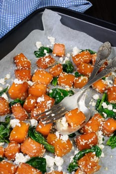 Slices of pumpkin baked with spinach and sesame seeds on a baking sheet